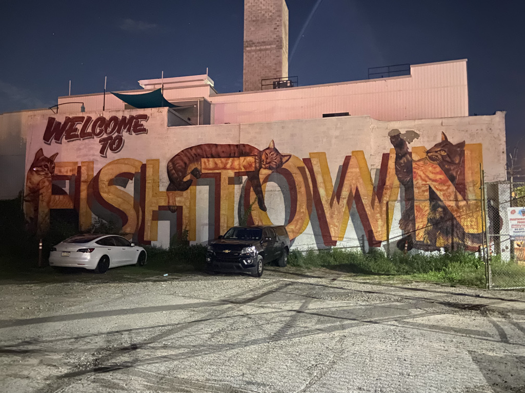 A mural that says "Welcome to Fishtown". In the mural, there is a cat sitting behind the F, a cat laying on top of the T, and a cat sitting behind the N.