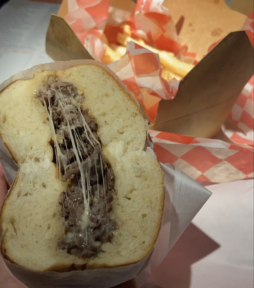 A cheesesteak sandwich with beef and melted cheese. A basket of fries are in the background.