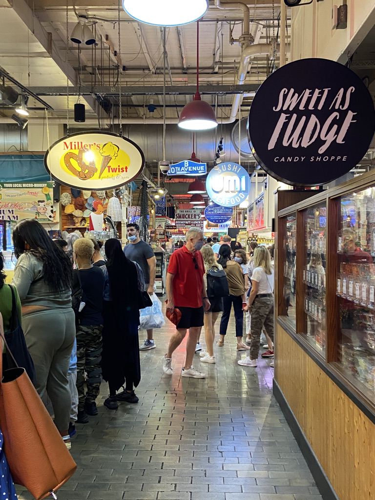 The interior of Reading Terminal Market - a narrow corridor filled with people and store signs. The two closest signs read "Sweet as Fudge Candy Shoppe" and "Miller's Twist"