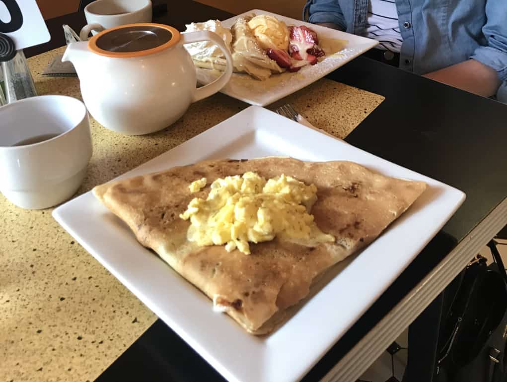 Brunch at Chez Elle. Two plates of crepes and a pot and two cups filled with coffee. The crepe closest to the photographer has eggs on top, and the other crepe has strawberries and vanilla ice cream on top.