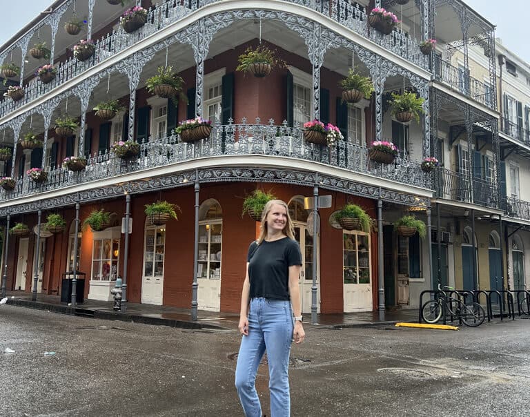 Stephanie (the author of this blog) wearing a black shirt and jeans standing in front of a French-style building.
