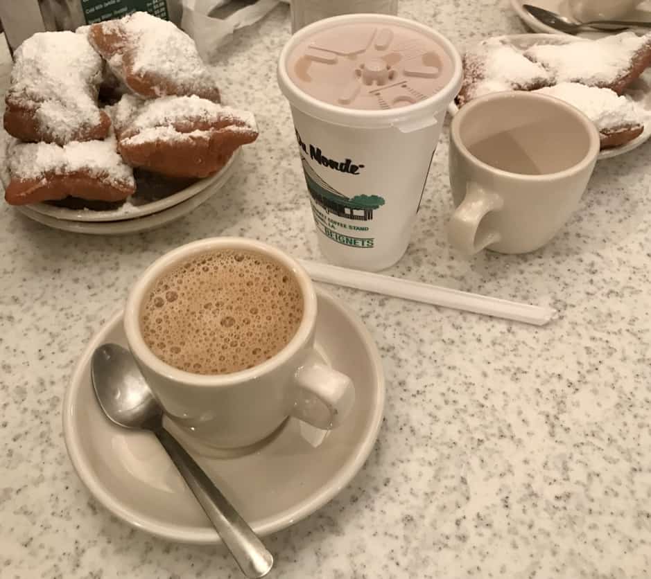 Two plates of four beignets each accompanied with two cups of coffee