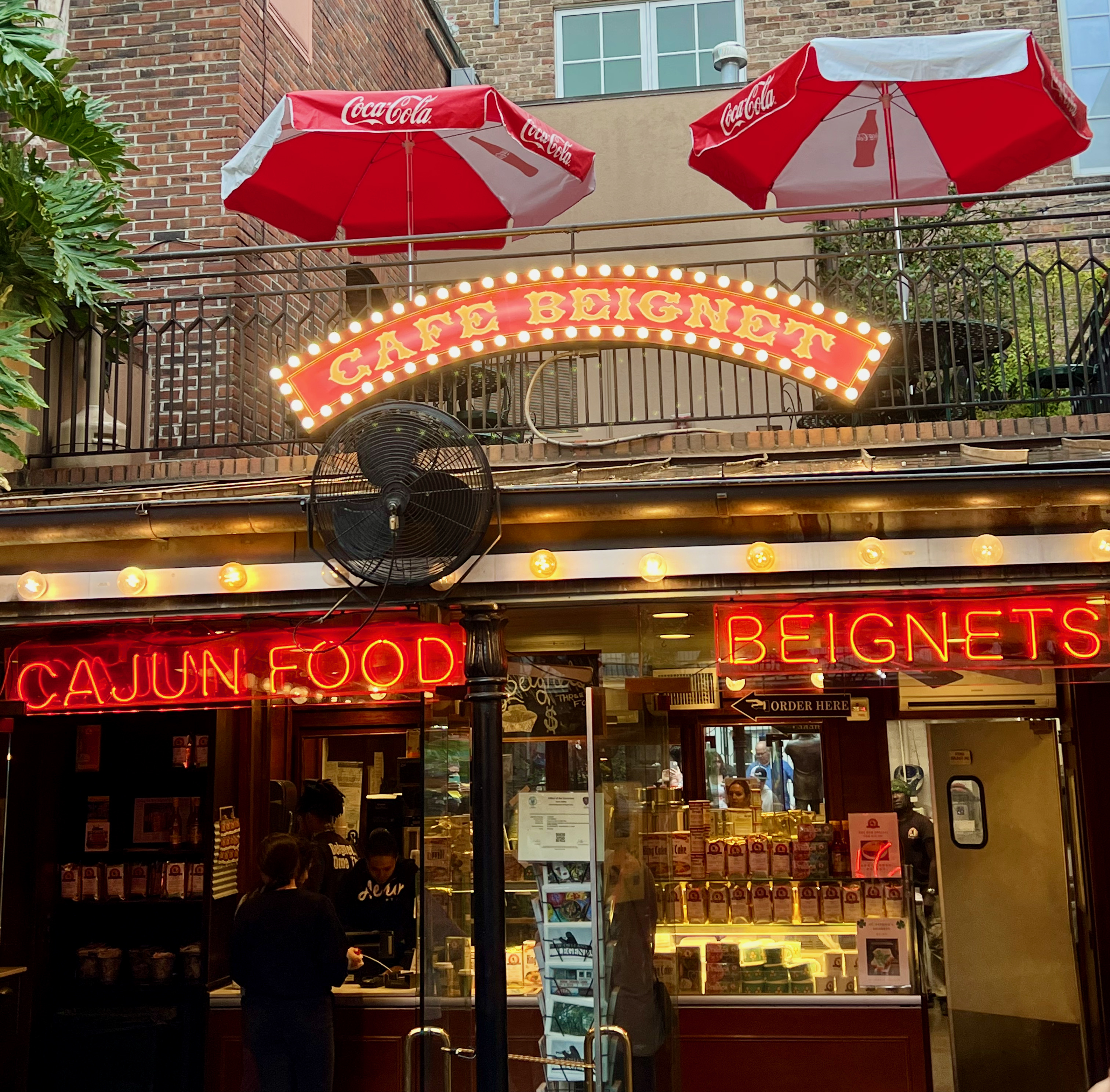 The entrance to Café Beignet on Bourbon St, which is adorned with a bright red sign that says "Cafe Beignet" and two red neon signs below it that say Cajun Food and Beignets