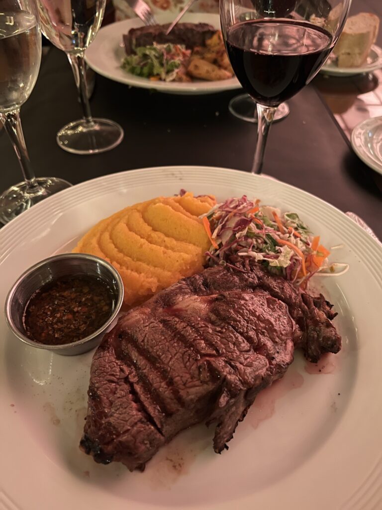 A large steak with a side of chimichurri sauce, coleslaw, and mashed sweet potatoes.