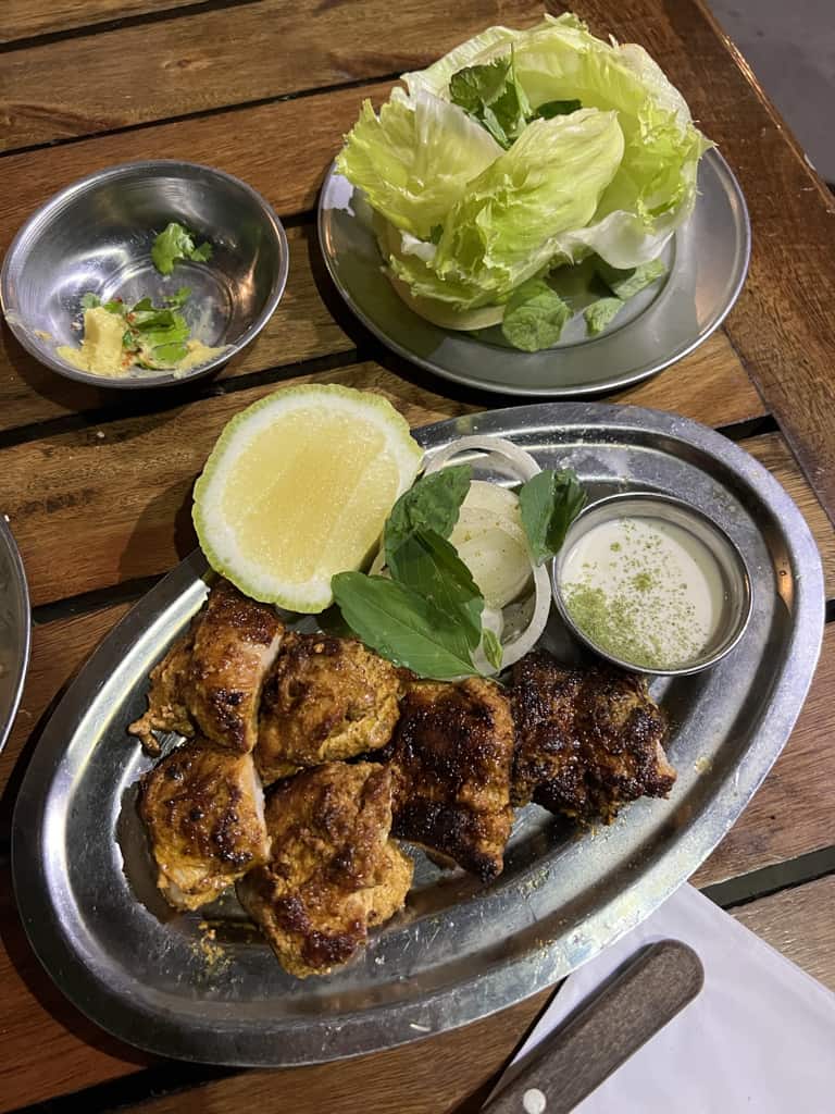 A plate of pork paired with half a lemon and some dipping sauce. A plate of lettuce is beside the dish.
