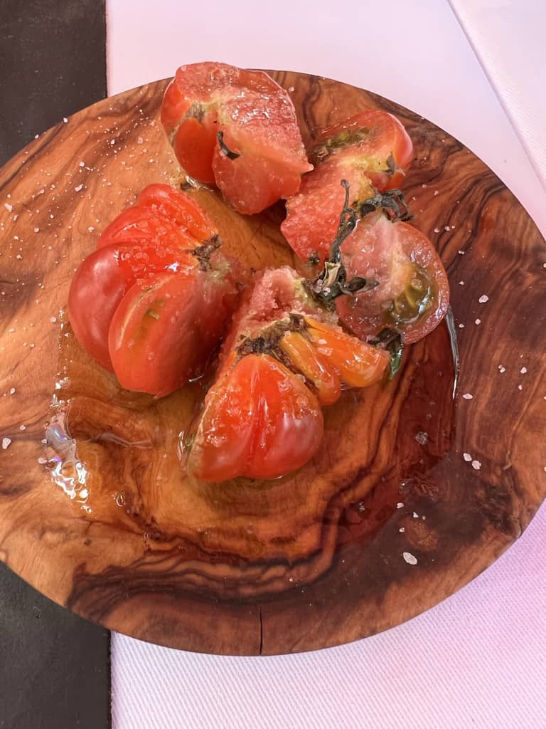 A wooden board topped with sliced tomatoes garnished with salt and olive oil
