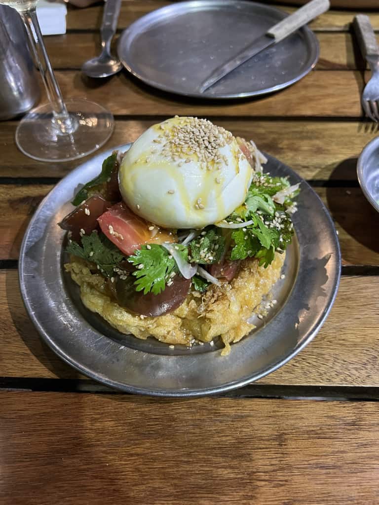 A chickpea bread topped with various garnishing and a poached egg