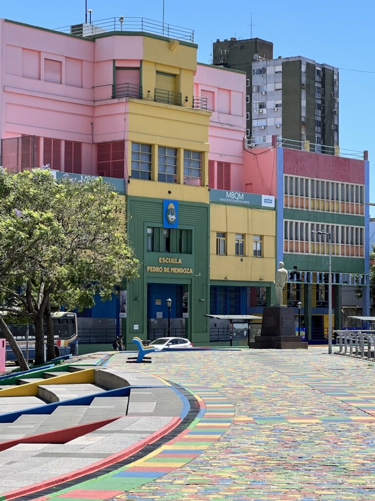 A schoolhouse and police station are painted very brightly in pink, yellow, green, and red. A street with matching bright colors leads to these buildings.