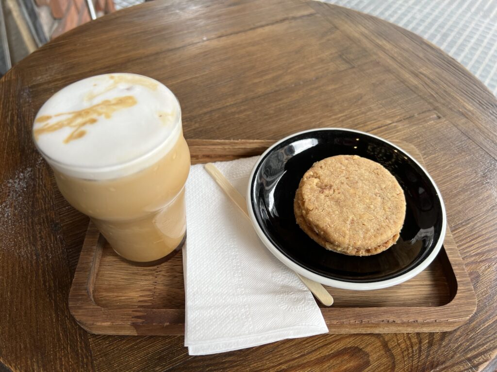 A latte and alfajor pastry on top of a wooden board, which is placed on a wooden table.