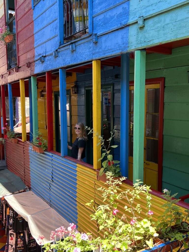 Stephanie (the author of this post) is looking off the balcony of a multi-story building. The building is painted a variety of bright colors including blue, yellow, teal, and red.