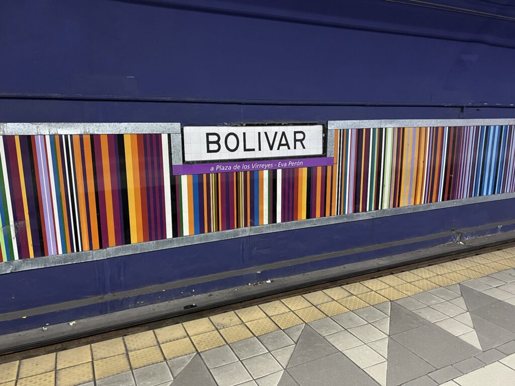 A subway station with a purple wall with rainbow stripes in the middle