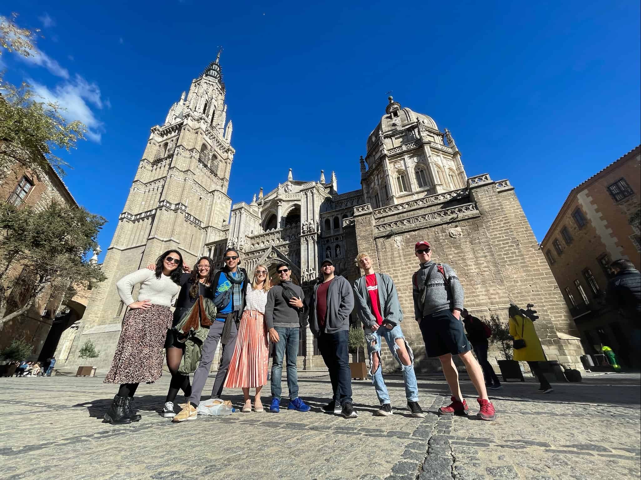 A group of eight travelers standing in front of a church in Toledo, Spain on a sunny day.